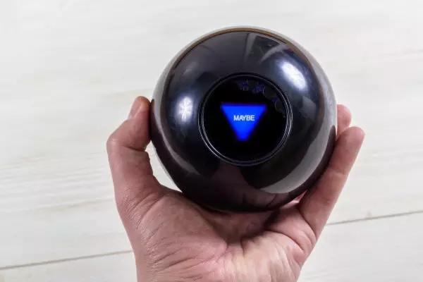 Magic prediction eight ball in hand, on the white wooden background that says "Maybe"